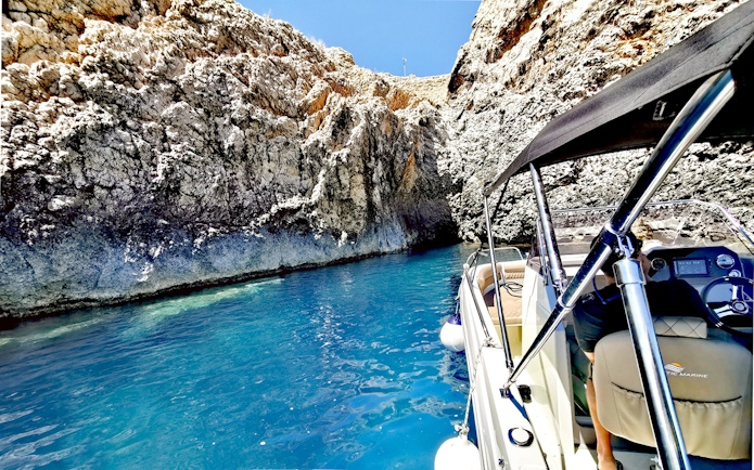 Boat entering a blue cave with rocky walls and clear water.
