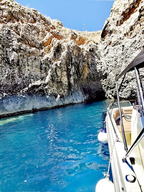 Boat entering a blue cave with rocky walls and clear water.