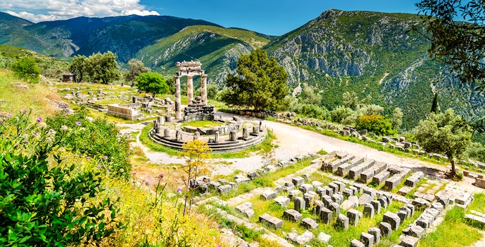 Tholos of Athena Pronaia in Delphi with surrounding ruins and mountainous landscape.