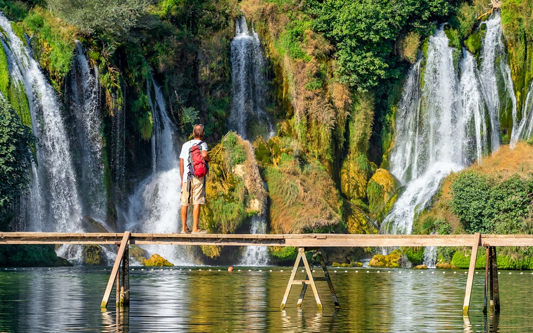 Tourist on wooden bridge in front of Kravica waterfall, Bosnia and Herzegovina.