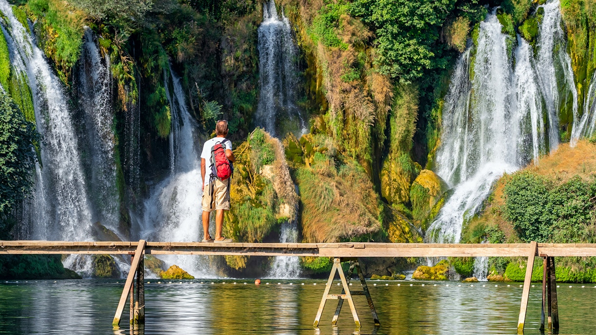 Tourist on wooden bridge in front of Kravica waterfall, Bosnia and Herzegovina.