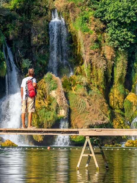 Tourist on wooden bridge in front of Kravica waterfall, Bosnia and Herzegovina.