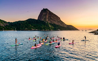Group paddleboarding at sunrise near Sugarloaf Mountain, Rio de Janeiro.