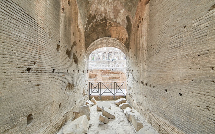 Archway passage in the underground Colosseum, Rome, with ancient stone walls and scattered ruins.