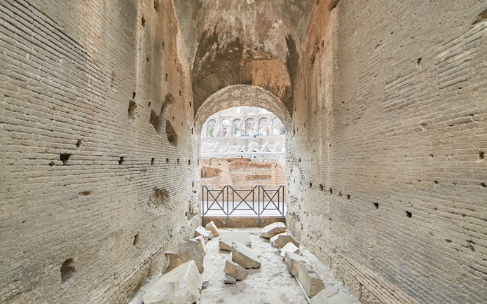 Archway passage in the underground Colosseum, Rome, with ancient stone walls and scattered ruins.