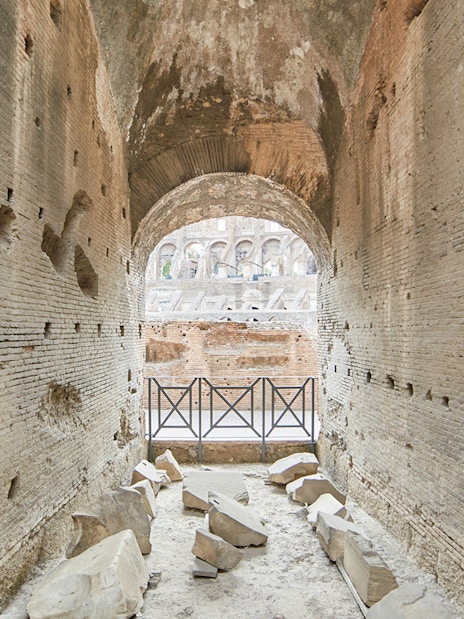 Archway passage in the underground Colosseum, Rome, with ancient stone walls and scattered ruins.