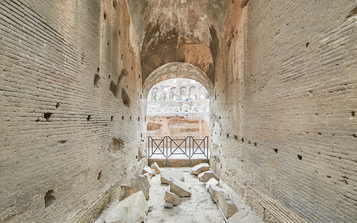 Archway passage in the underground Colosseum, Rome, with ancient stone walls and scattered ruins.