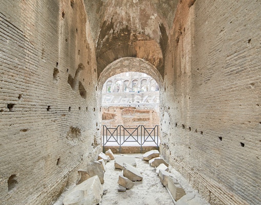 Archway passage in the underground Colosseum, Rome, with ancient stone walls and scattered ruins.