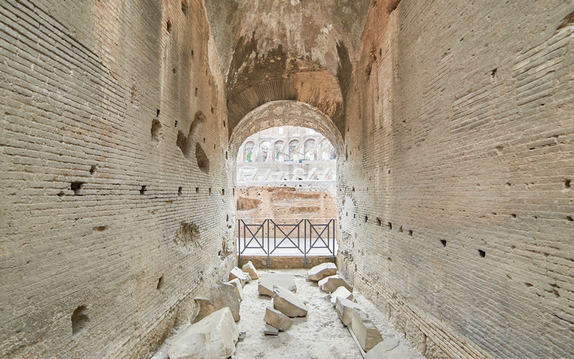 Archway passage in the underground Colosseum, Rome, with ancient stone walls and scattered ruins.