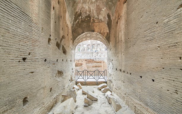 Archway passage in the underground Colosseum, Rome, with ancient stone walls and scattered ruins.