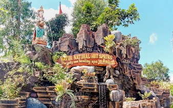 Batur Natural Hot Spring entrance sign with statue and lush greenery in Bali.