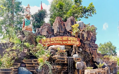 Batur Natural Hot Spring entrance sign with statue and lush greenery in Bali.
