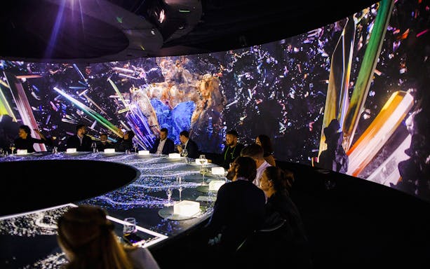 Guests seated at a circular table with immersive digital art projections at IMAGINARY ART show, KRASOTA Dubai.