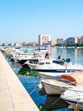 Boats docked at the port in Zadar, Croatia with city buildings in the background.