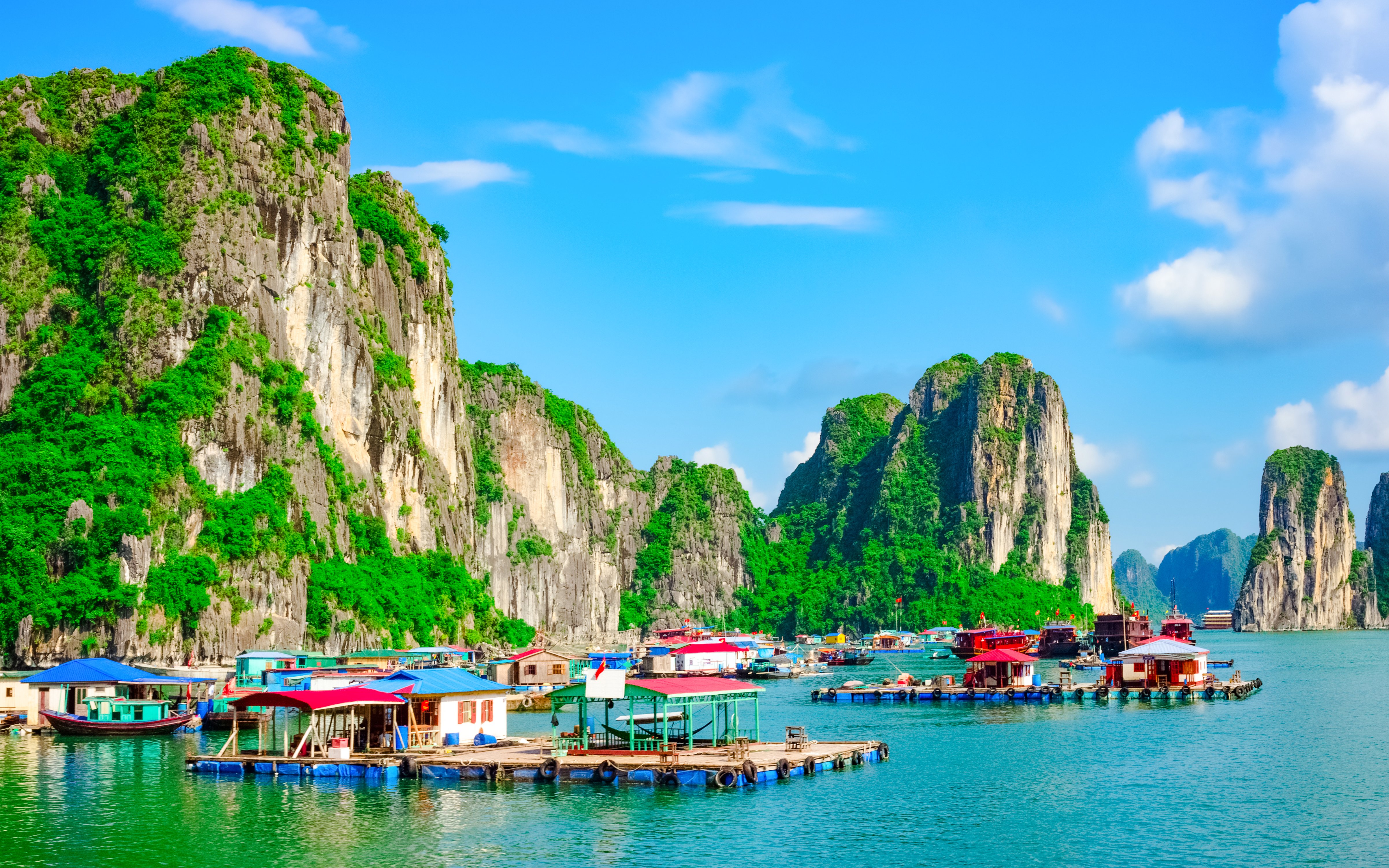 Floating villages with colorful houses on water in Ha Long Bay, surrounded by limestone cliffs.