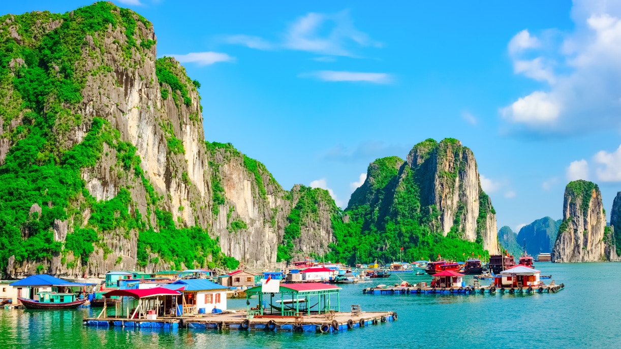Floating villages with colorful houses on water in Ha Long Bay, surrounded by limestone cliffs.