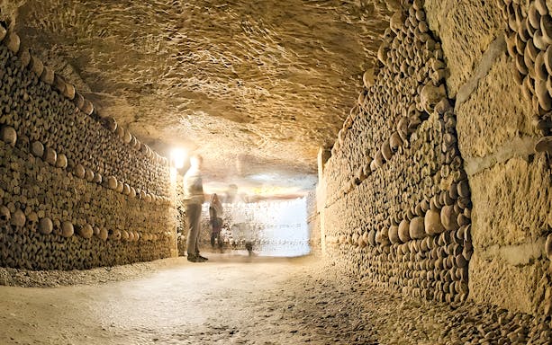 Visitors walking through the bone-lined corridors of the Catacombs of Paris.