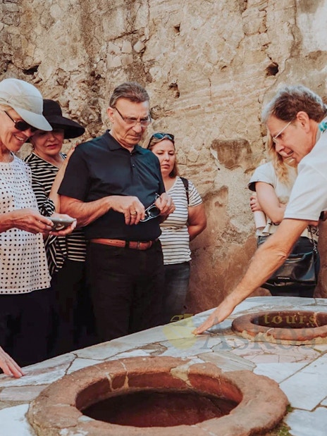 Group listening to archaeologist during Herculaneum guided tour, examining ancient ruins.