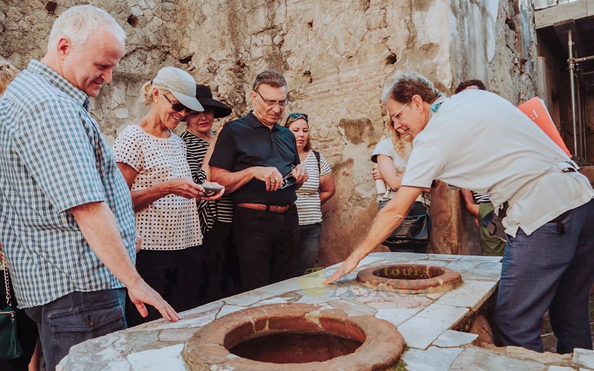 Group listening to archaeologist during Herculaneum guided tour, examining ancient ruins.