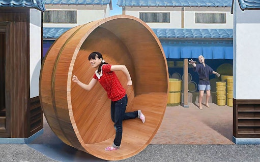 Person in a red shirt inside a large wooden wheel at Tokyo Trick Art Labyrinth Museum.