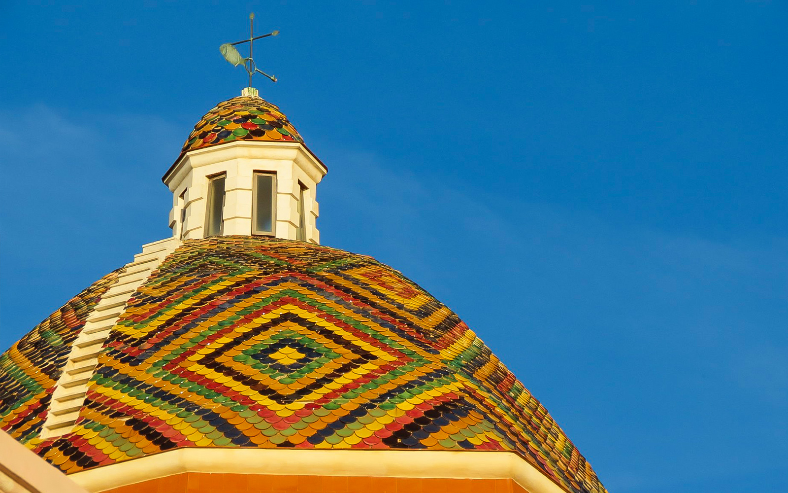 Colorful tiled dome of Alghero Cathedral against blue sky, Alghero Historic Center.
