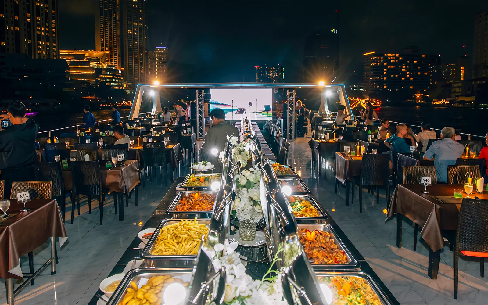 Buffet setup on a dinner cruise in Bangkok with city skyline views.