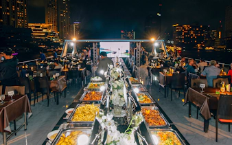 Buffet setup on a dinner cruise in Bangkok with city skyline views.