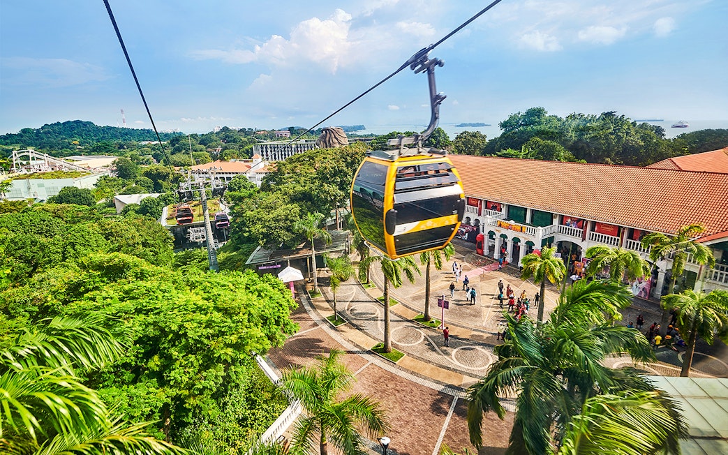 Cable cars over Sentosa Island with Singapore skyline in the background.