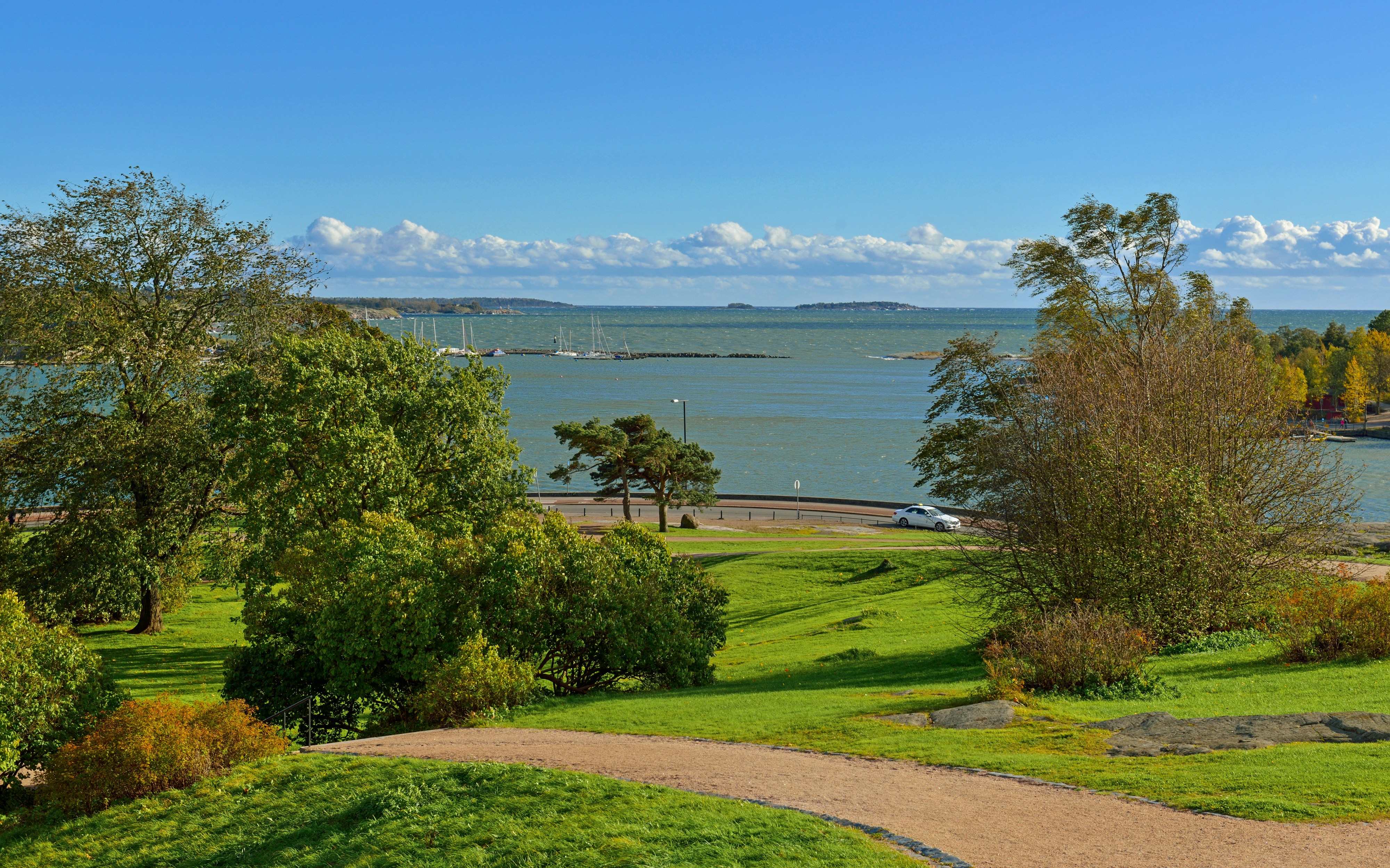 Kaivopuisto park overlooking the Gulf of Finland in Helsinki, with lush greenery and distant sailboats.