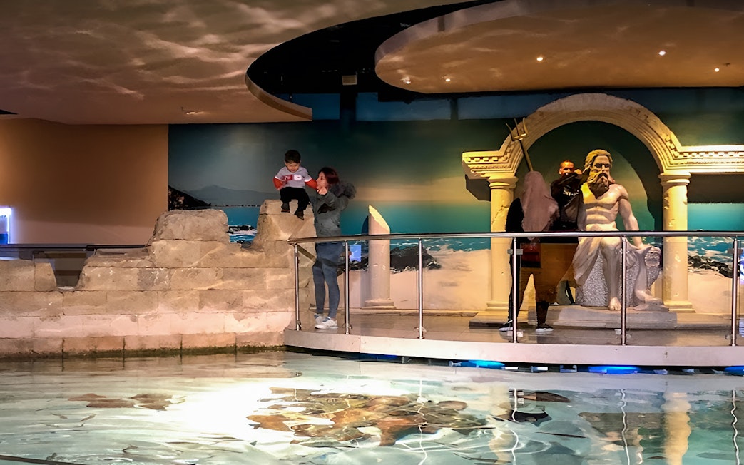 Visitors exploring the Istanbul Aquarium near a Poseidon statue.