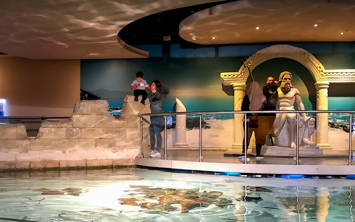 Visitors exploring the Istanbul Aquarium near a Poseidon statue.