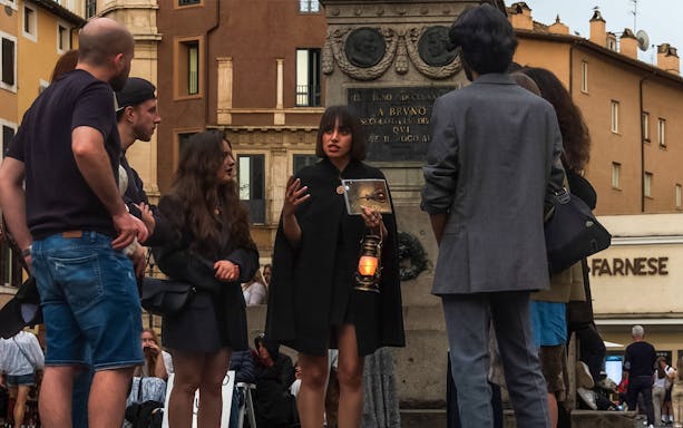 Tour guide with lantern leading tourists on legend and ghosts of Rome tour near statue.