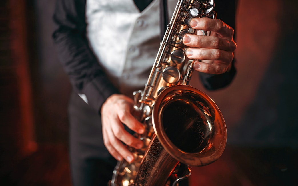 Saxophonist playing a brass saxophone in a dimly lit setting.
