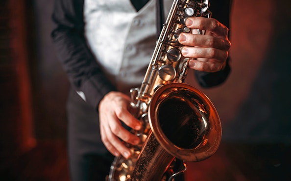 Saxophonist playing a brass saxophone in a dimly lit setting.