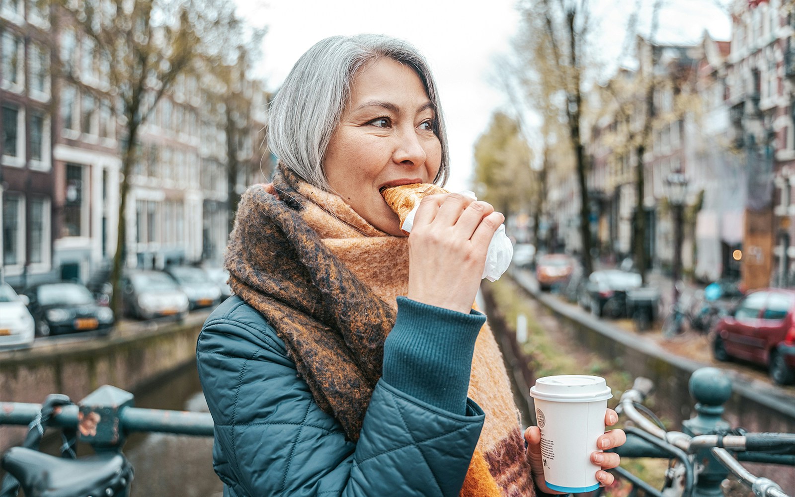 Person enjoying a pastry and coffee on a canal bridge during a self-guided food tour in Amsterdam's Jordaan District.