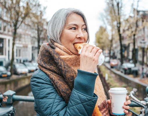 Person enjoying a pastry and coffee on a canal bridge during a self-guided food tour in Amsterdam's Jordaan District.