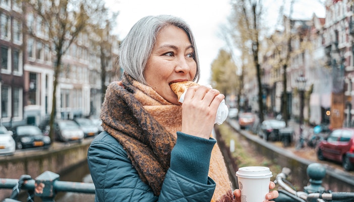 Person enjoying a pastry and coffee on a canal bridge during a self-guided food tour in Amsterdam's Jordaan District.