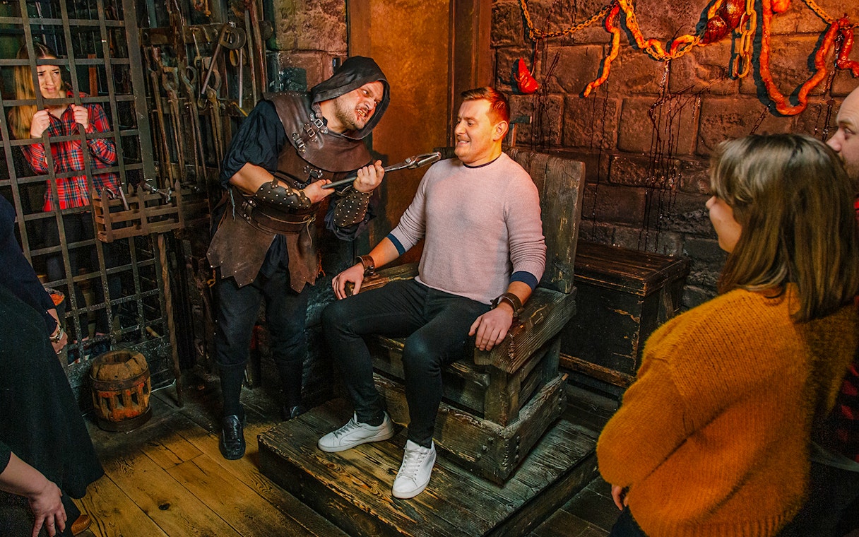 Torturer interacting with a visitor in the London Dungeon torture chamber exhibit.