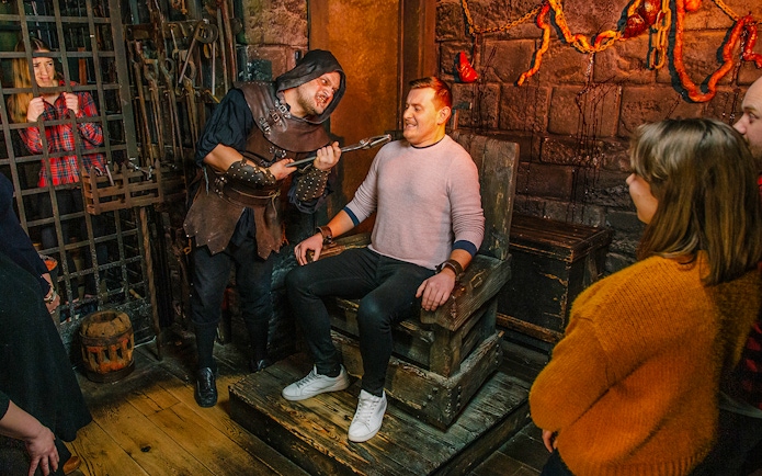Torturer interacting with a visitor in the London Dungeon torture chamber exhibit.