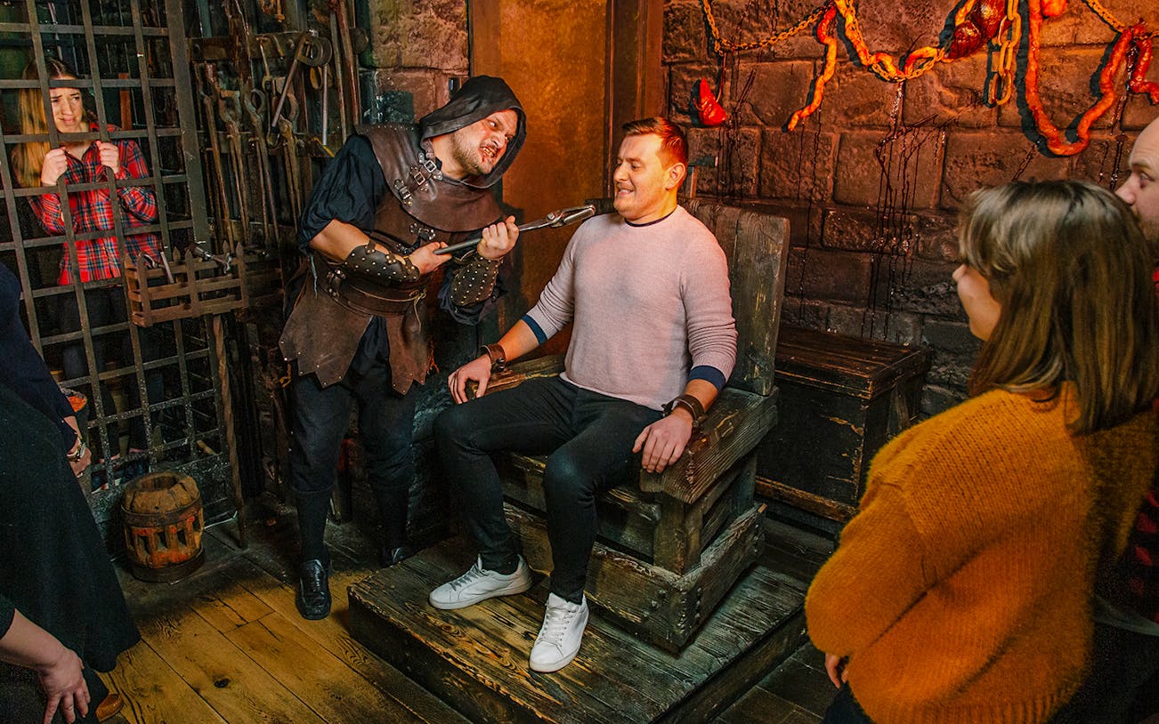 Torturer interacting with a visitor in the London Dungeon torture chamber exhibit.