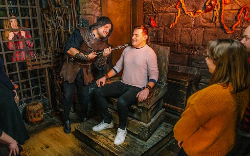 Torture scene reenactment at London Dungeon with visitors watching.
