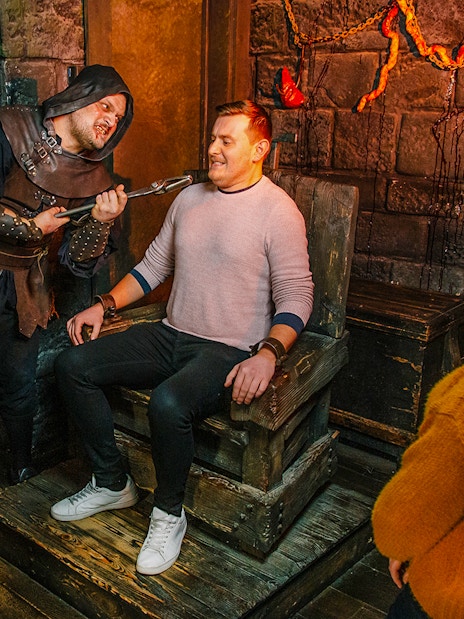 Torture scene reenactment at London Dungeon with visitors watching.