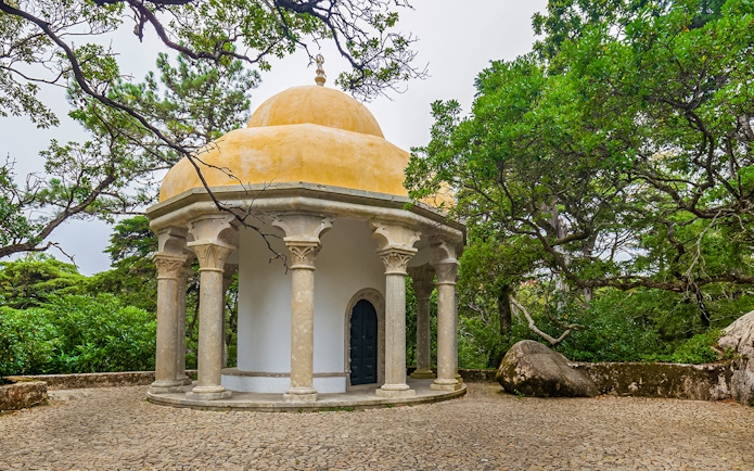 Columned temple at Pena Palace surrounded by lush greenery in Sintra, Portugal.