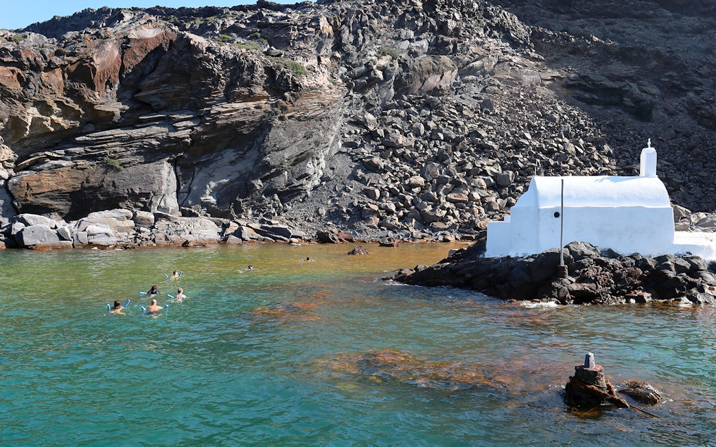 Swimmers enjoying hot springs near a white chapel at Palea Kameni, Santorini.