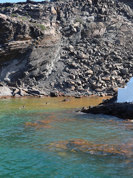Swimmers enjoying hot springs near a white chapel at Palea Kameni, Santorini.