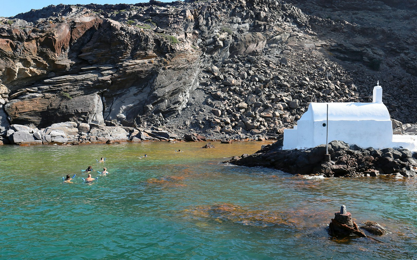 Tourists swimming in the hot springs at Palea Kameni, Santorini, with volcanic landscape in the background.