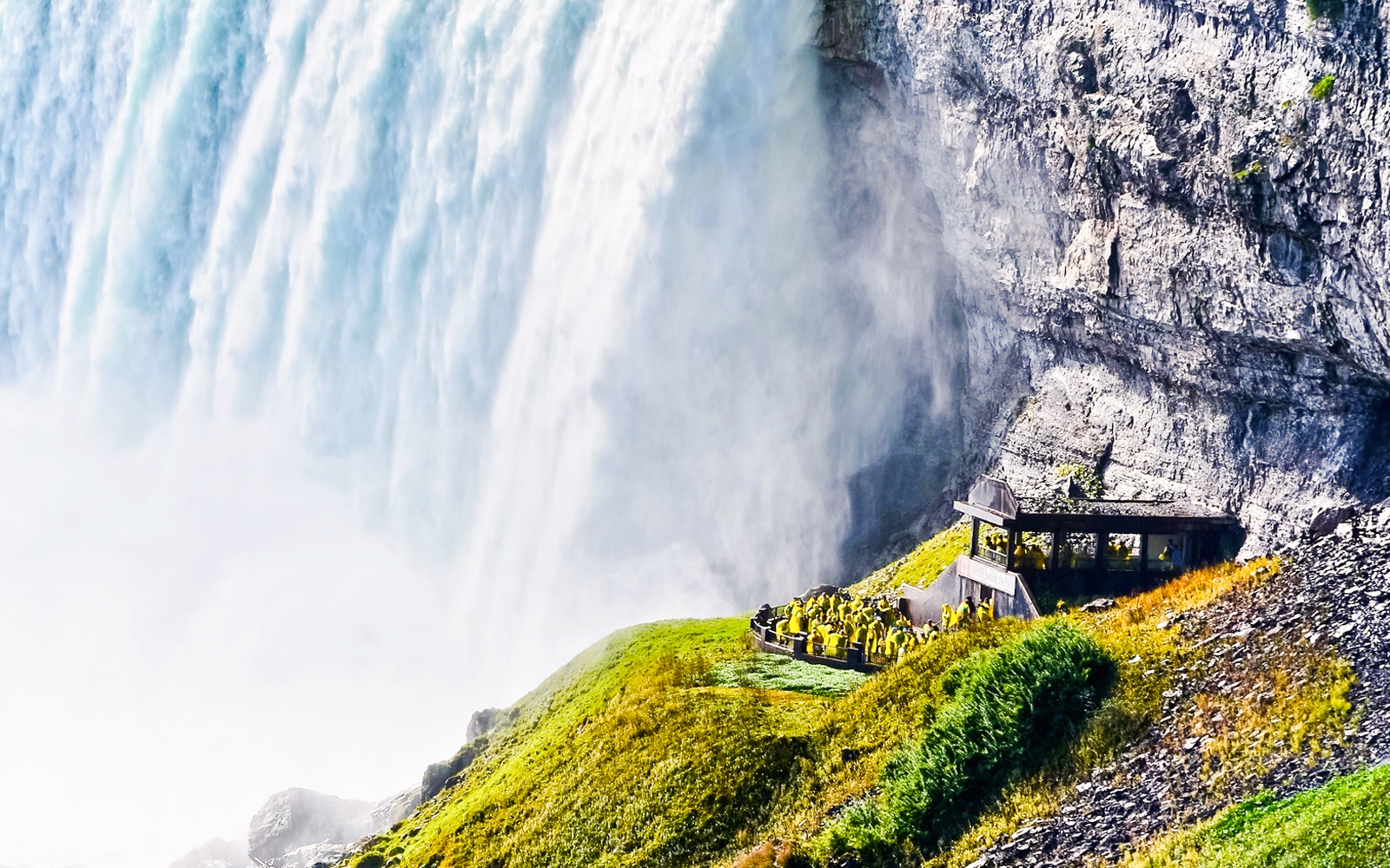 Visitors in raincoats at Niagara Falls observation deck, viewing cascading water.