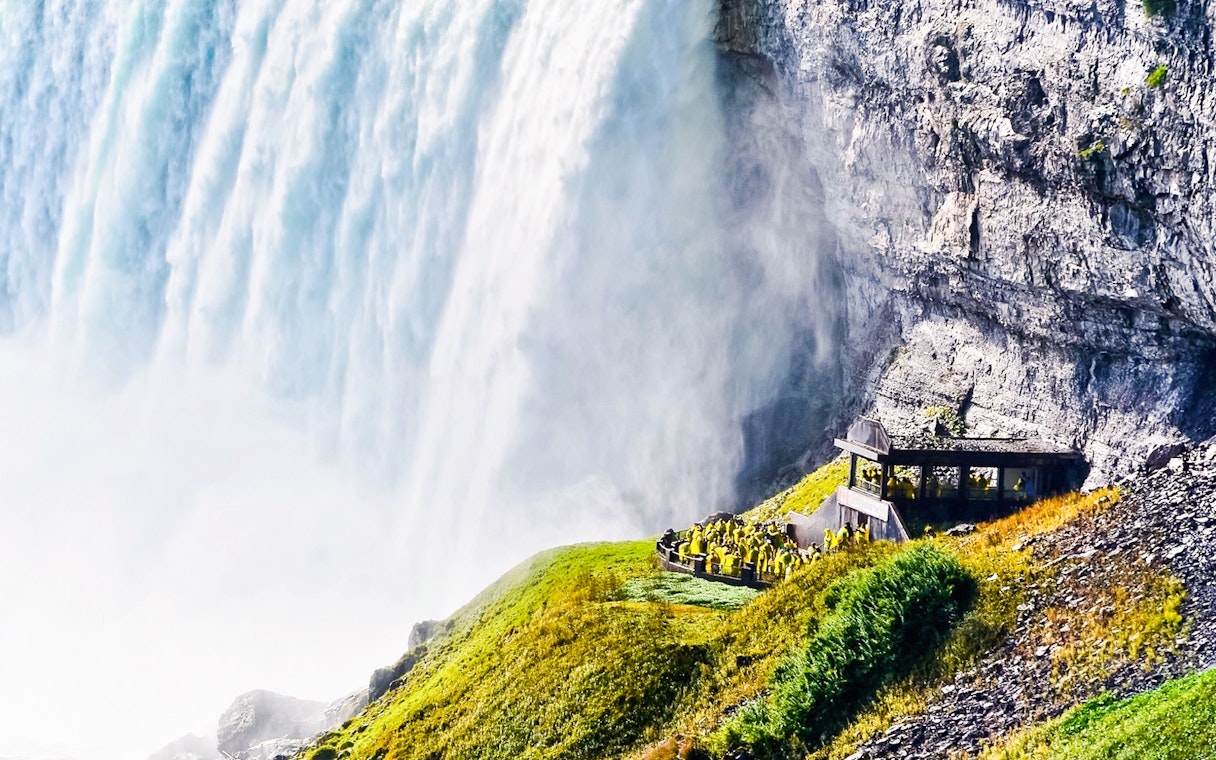 Visitors in raincoats at Niagara Falls observation deck, viewing cascading water.