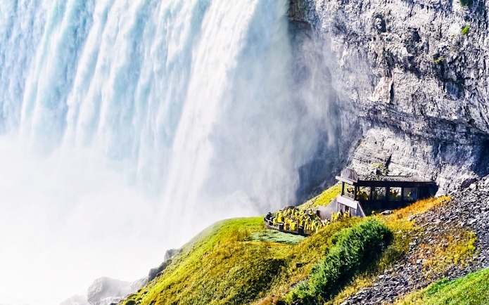 Visitors in raincoats at Niagara Falls observation deck, viewing cascading water.
