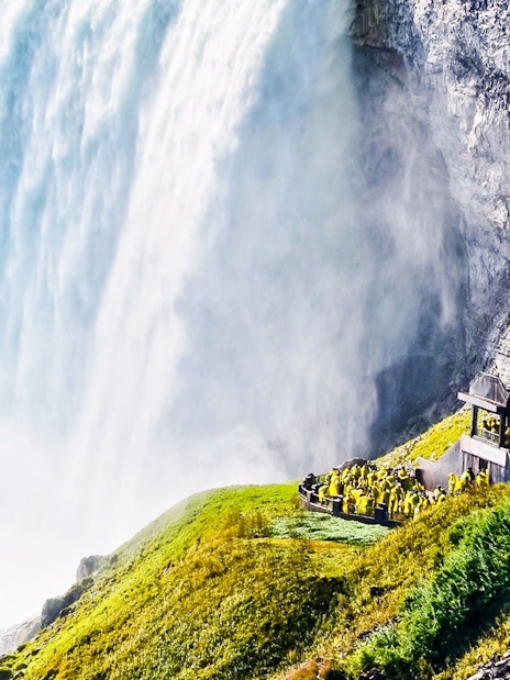 Visitors in raincoats at Niagara Falls observation deck, viewing cascading water.